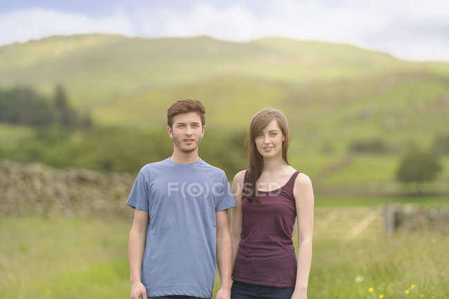 Teenage couple standing together in meadow and looking away over rural landscape — Stock Photo
