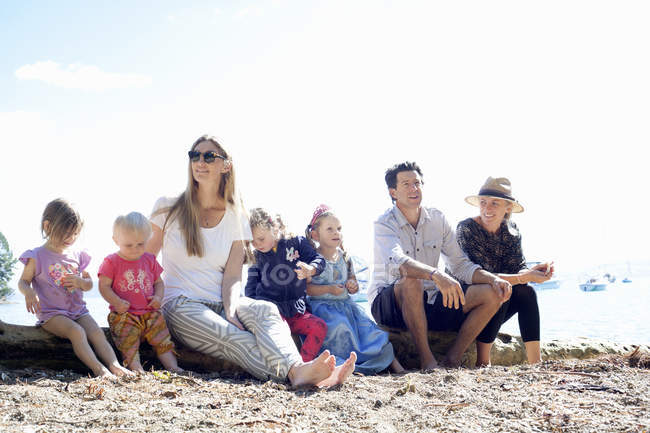 Famílias e filhas sentadas em tronco de árvore na praia, Nova Zelândia — Fotografia de Stock