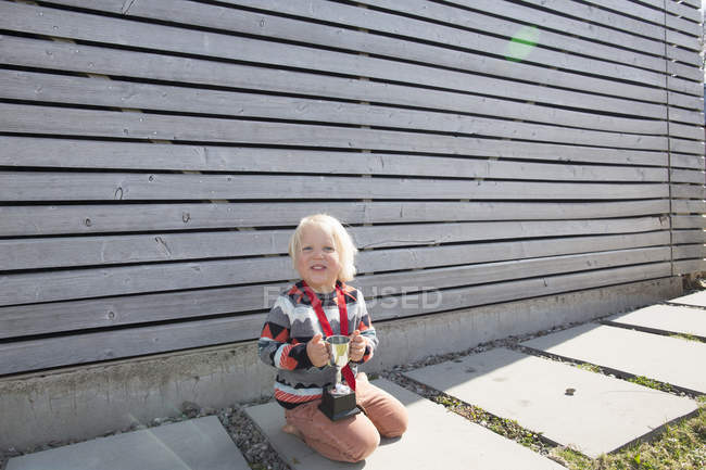 Boy holding a trophy while sitting on floor outdoors in garden — Stock Photo