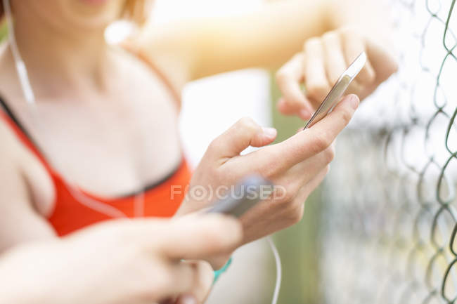 Young women using smartphone beside fence — Stock Photo
