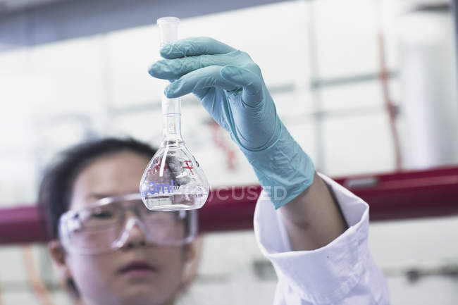 Female scientist holding up volumetric flask in lab — Stock Photo