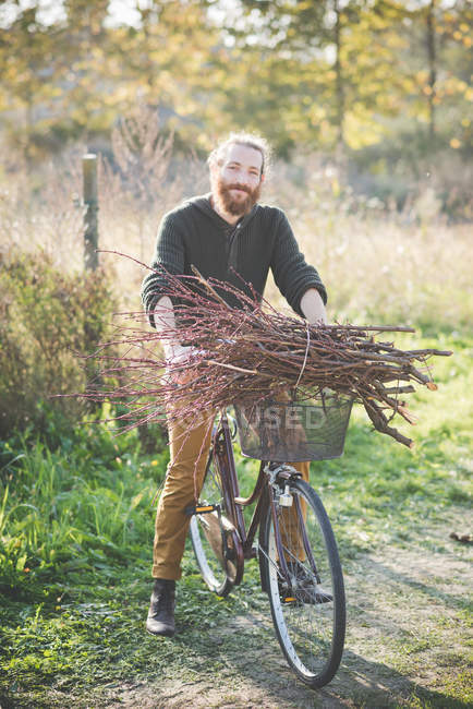 Jeune homme portant un tas de bâtons sur le vélo — Photo de stock