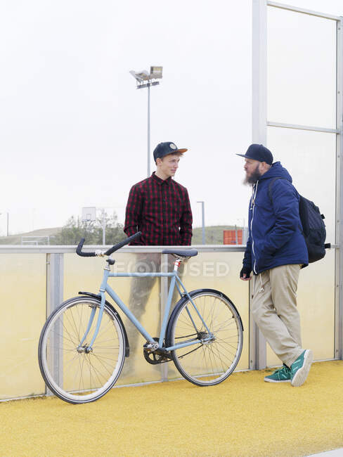 Ciclistas urbanos conversando por cerca no campo esportivo — Fotografia de Stock