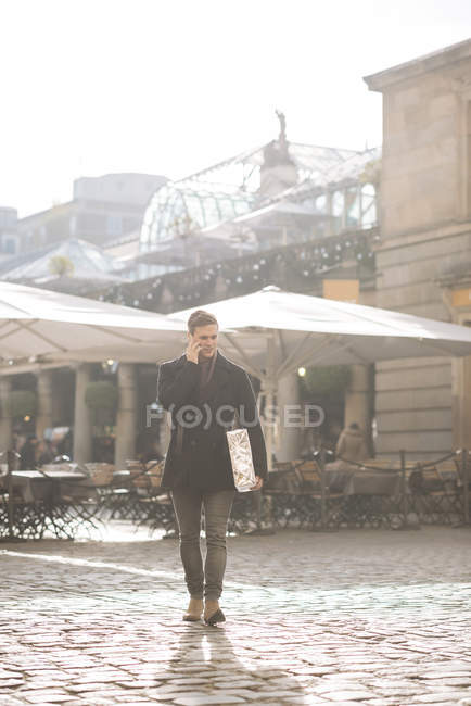 Jeune homme portant cadeau et bavardage sur smartphone à Covent Garden, Londres, Royaume-Uni — Photo de stock