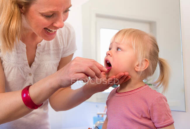 Madre cepillándose los dientes de la hija pequeña - foto de stock