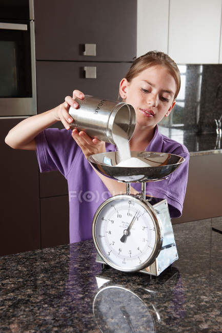 Menina pesando açúcar em balanças de cozinha — Fotografia de Stock