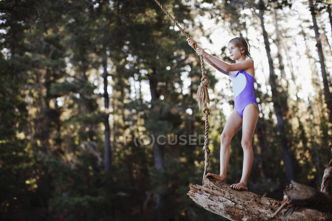Young girl using rope swing over lake — Stock Photo