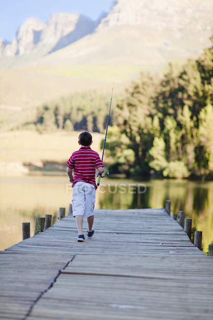 Garçon avec canne à pêche sur la jetée sur le lac — Photo de stock