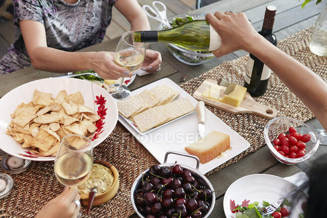Обрезанный вид сверху на подруг, наливающих вино за обеденным столом — стоковое фото