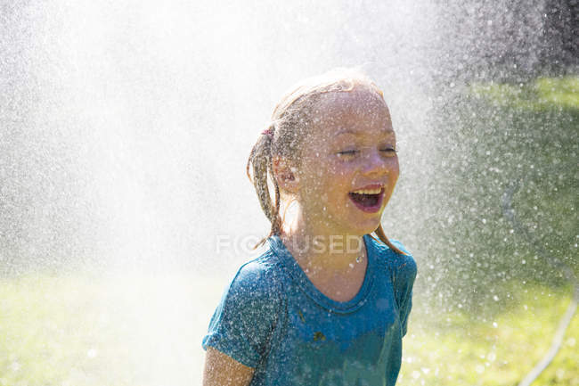 Girl getting splashed by water sprinkler in garden — Stock Photo