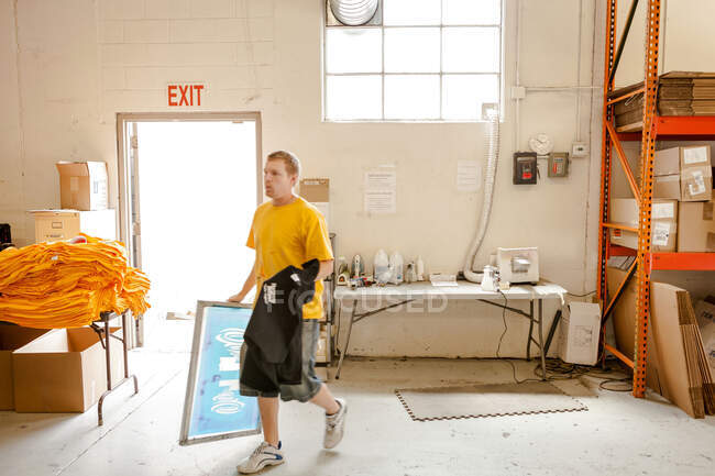 Travailleur portant cadre et t-shirt en atelier de sérigraphie — Photo de stock