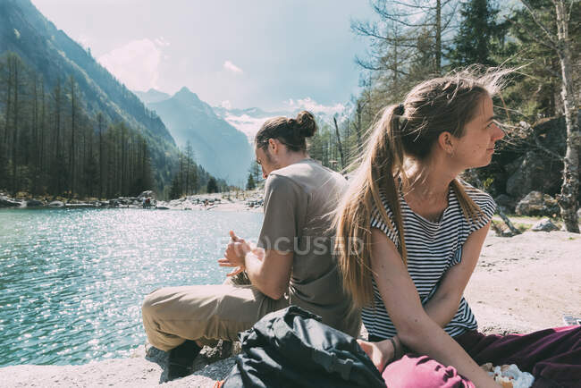 Two young adult hikers sitting by mountain lake, Lombardy, Italy — Stock Photo
