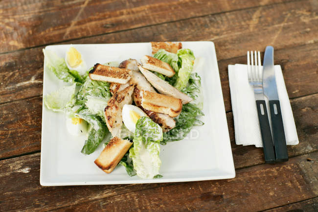 Тарілка хліба і салату, ніж і виделка на дерев'яному столі на кухні — стокове фото