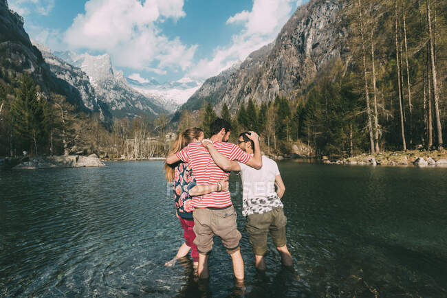 Rear view of three young adult friends ankle deep in mountain lake, Lombardy, Italy — Stock Photo