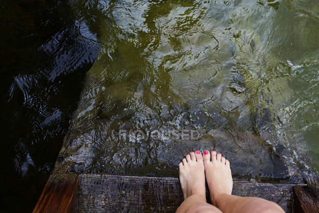 Pés femininos na borda do cais de madeira pela água — Fotografia de Stock