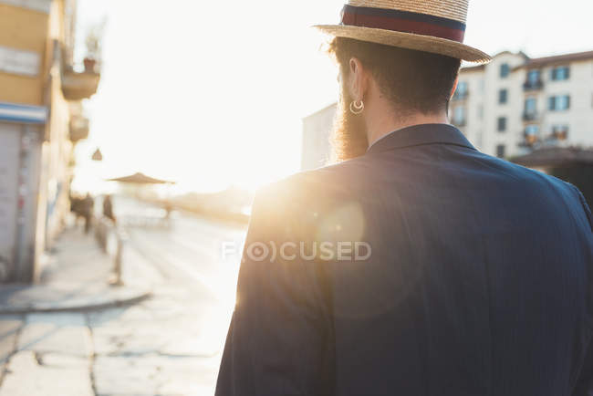 Rear view of man in boater strolling along sunlit street — Stock Photo