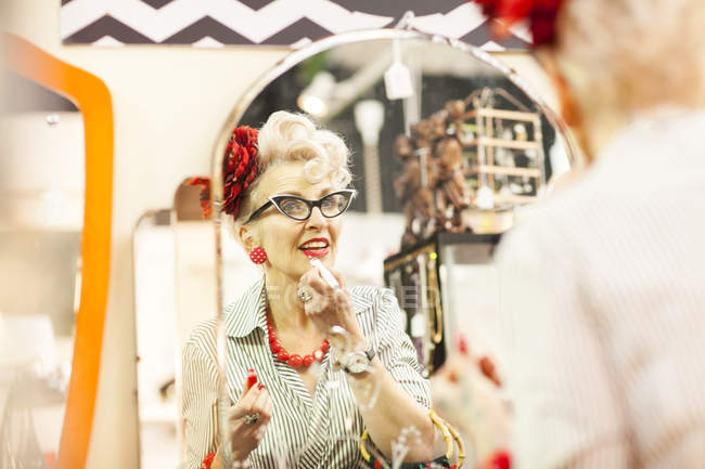 Mirror image of quirky vintage woman applying lipstick in antique and vintage emporium — Stock Photo