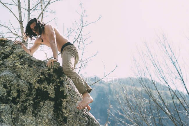 Mann mit nacktem Oberkörper und nacktem Fuß klettert auf Felsbrocken — Stockfoto