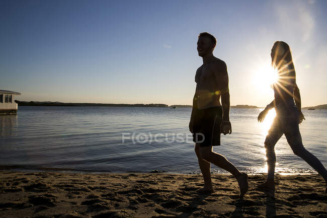 Backlit young man and girlfriend strolling on beach at sunset — Stock Photo