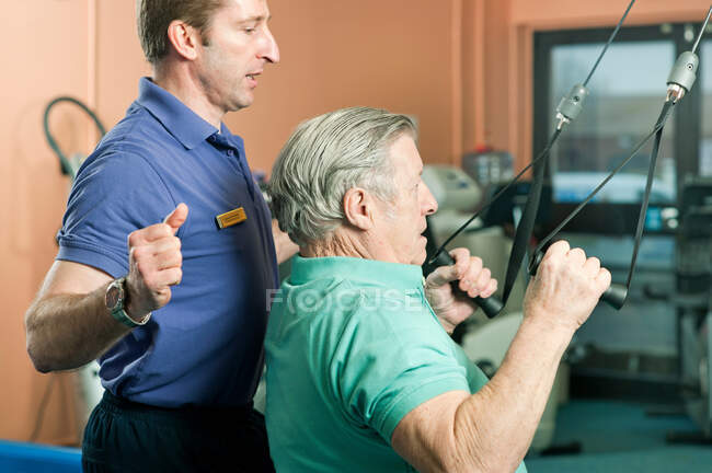 Trainer helping older man exercise — Stock Photo
