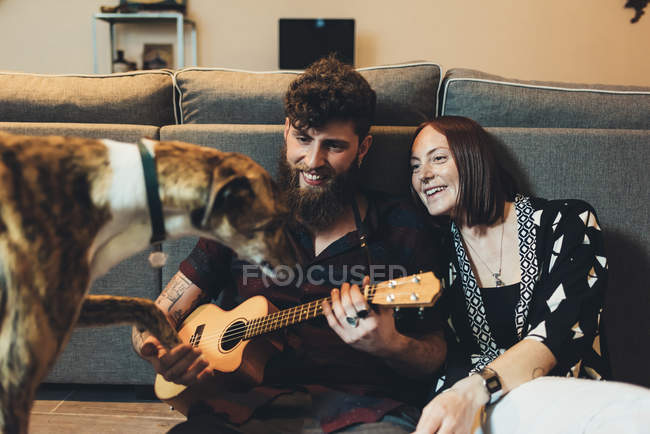 Couple assis sur le sol de l'appartement tenant la patte du chien — Photo de stock
