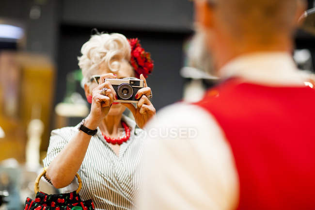 Quirky vintage woman photographing boyfriend on vintage camera in antiques emporium — Stock Photo