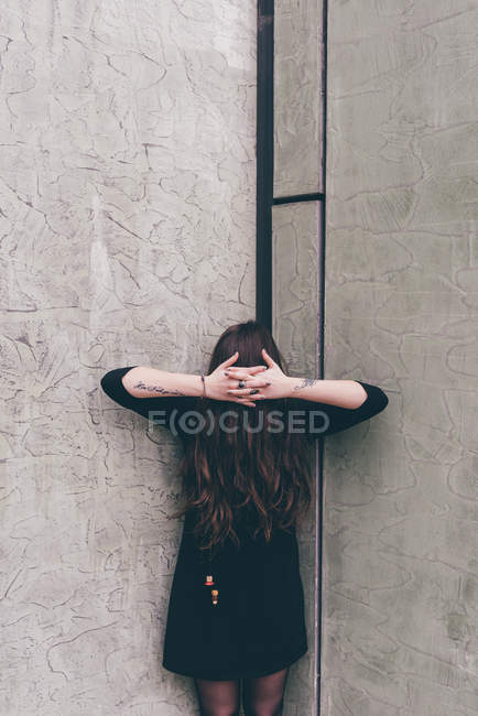 Portrait of young woman standing in corner, hair covering face, hands clasped in front of hair — Stock Photo