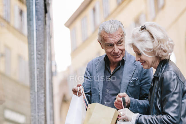 Pareja de turistas que buscan en bolsas de compras en la calle de la ciudad, Siena, Toscana, Italia - foto de stock