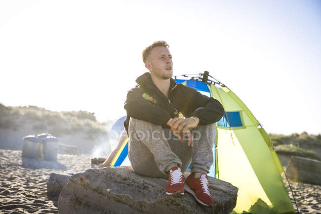 Giovane camper maschile seduto su roccia spiaggia — Foto stock