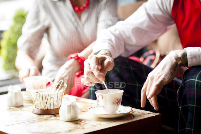 Закрытие рук пожилого человека, помешивающего чай в винтажных чайных комнатах — стоковое фото