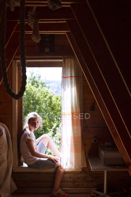Retrato de adolescente sentada en el alféizar de la ventana del dormitorio iluminado por el sol - foto de stock