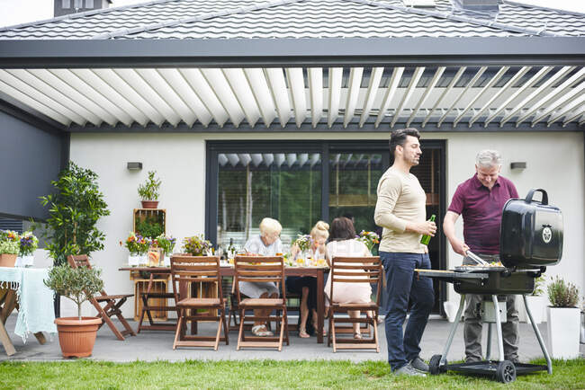 Deux hommes faisant un barbecue sur le patio au déjeuner en famille — Photo de stock