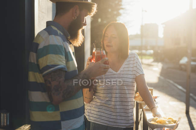 Coppia alzando un brindisi cocktail al caffè marciapiede illuminato dal sole — Foto stock