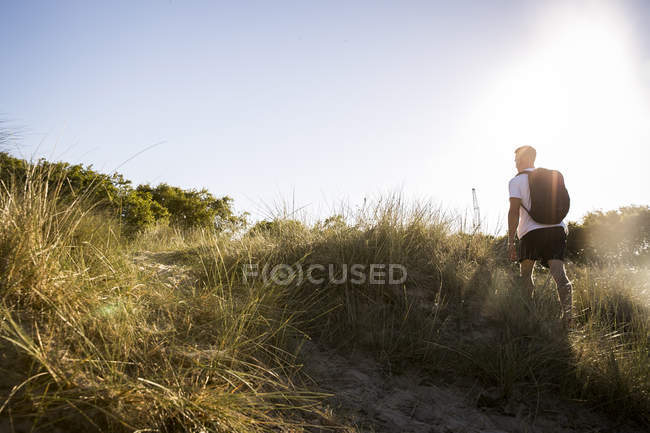Vista trasera del joven caminando a través de dunas de arena - foto de stock