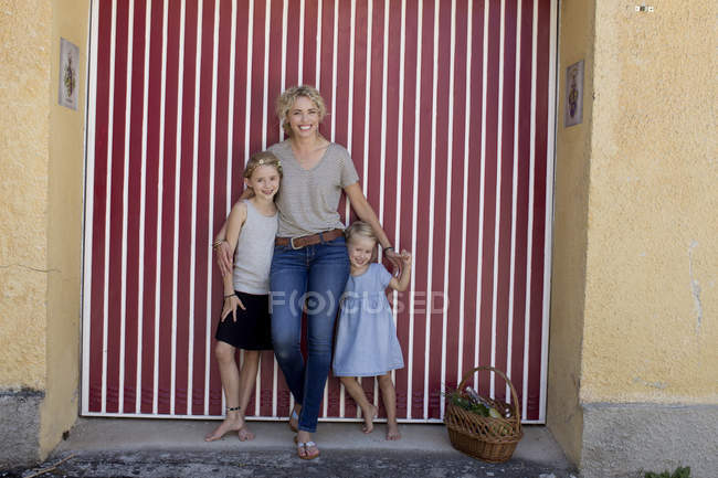 Mother and daughters standing by basket in front of door — Stock Photo