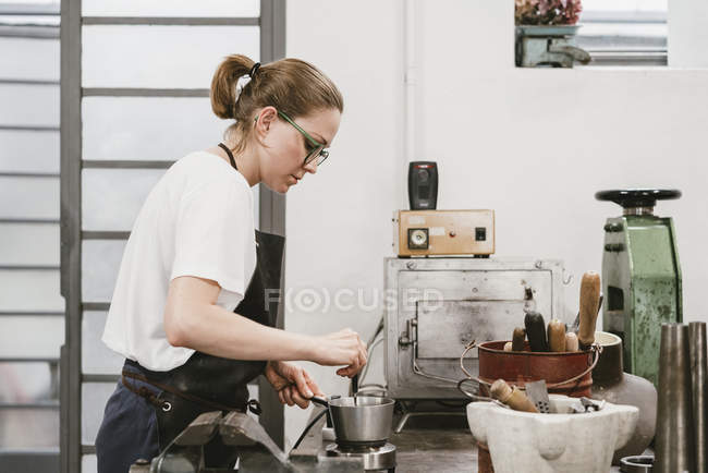 Side view of Female jeweler stirring molten metal in saucepan — Stock Photo