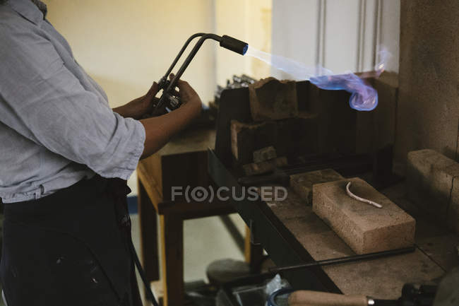 Sección media de joyera femenina usando antorcha de soplo en llamas en el banco de trabajo - foto de stock