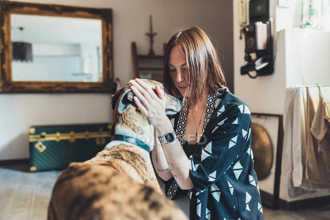 Mujer joven acariciando a su perro en apartamento - foto de stock