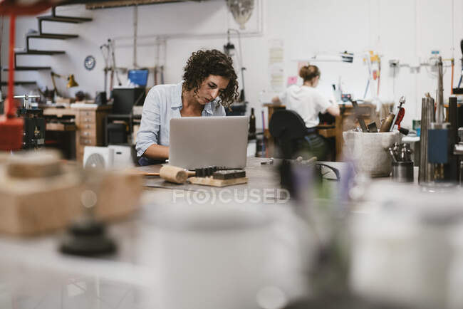 Female jeweller typing on laptop at workbench — Stock Photo