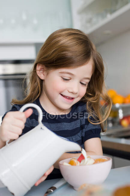 Chica poniendo leche en su tazón - foto de stock