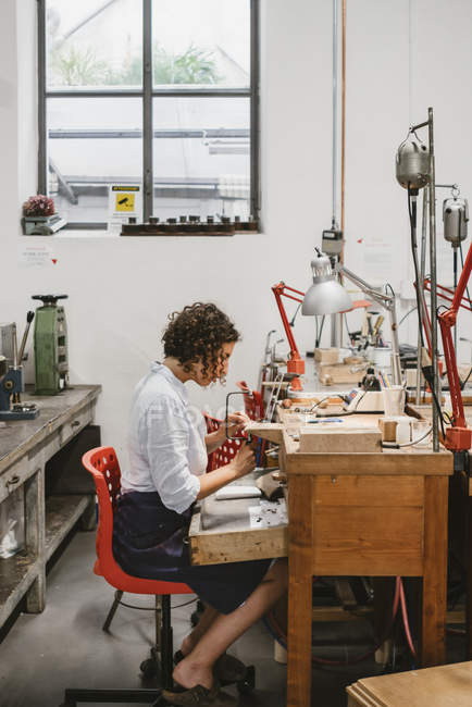 Female jeweler using coping saw at workbench — Stock Photo
