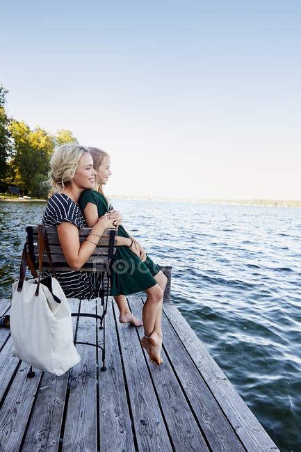 Madre e figlia seduti sul molo vicino all'acqua — Foto stock