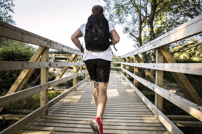 Rear view of young male running across rural footbridge — Stock Photo