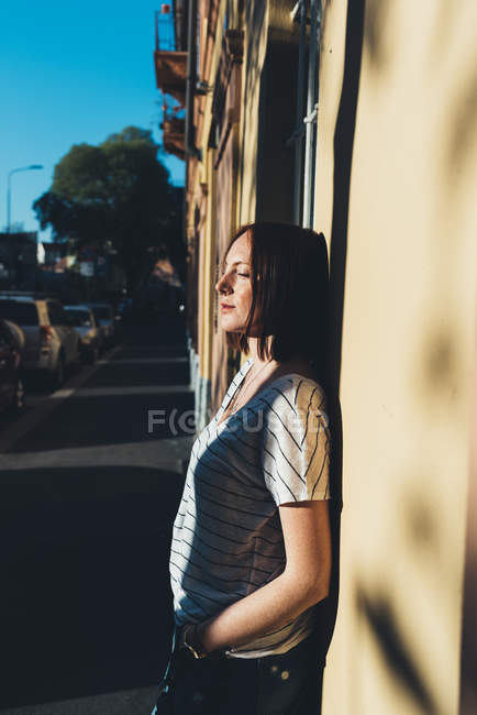 Giovane donna appoggiata alla parete illuminata dal sole — Foto stock