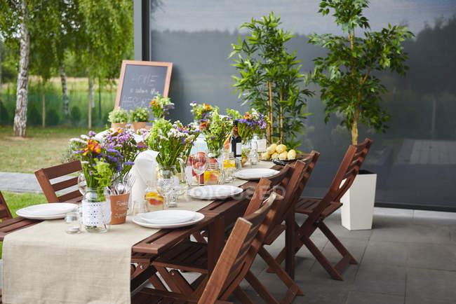 Стіл, приготований з квітковими композиціями та тарілками для обіду на патіо — стокове фото