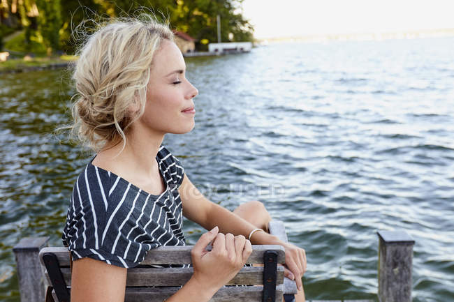 Frau sitzt auf Pier am Wasser — Stockfoto