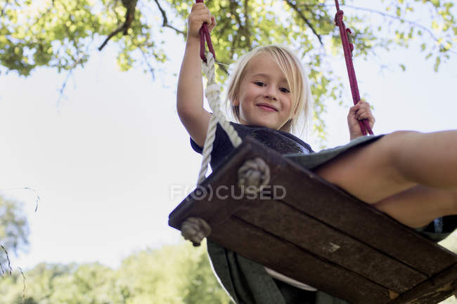 Девушка на качелях смотрит в камеру в парке — стоковое фото