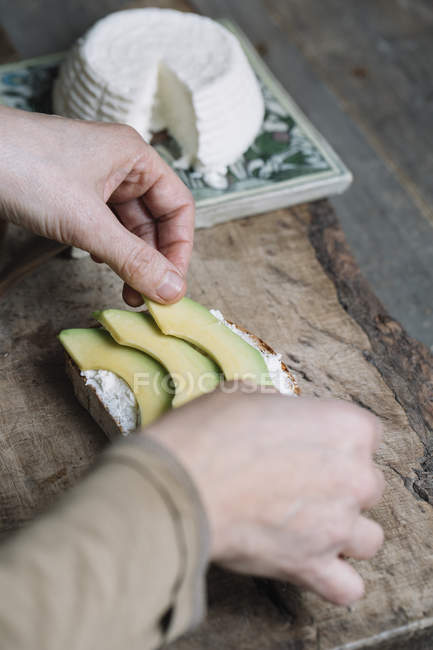 Woman placing slices of avocado onto sliced bread with ricotta, close-up — Stock Photo