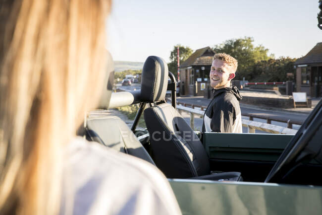 Sobre vista ombro de homem jovem e namorada com tração nas quatro rodas conversível no parque de estacionamento costeiro — Fotografia de Stock