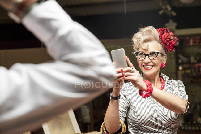 Quirky vintage woman photographing boyfriend in antiques emporium — Stock Photo